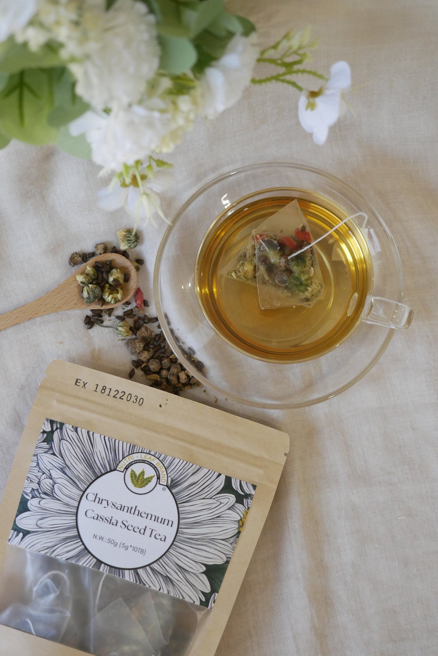 Tea cup with a teabag, wooden spoon, and flowers on a marble surface