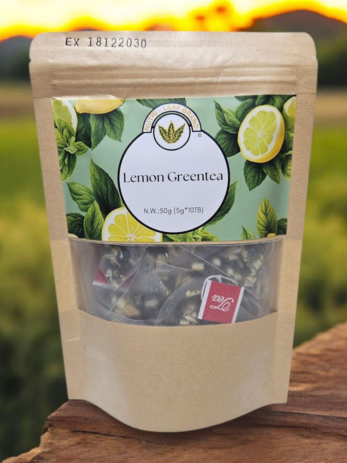 A standing pouch of Nutri-Leaf Brand Lemon Green Tea with a clear window showing tea leaves inside. The packaging is predominantly green with images of lemons and text detailing the product name and additional information.