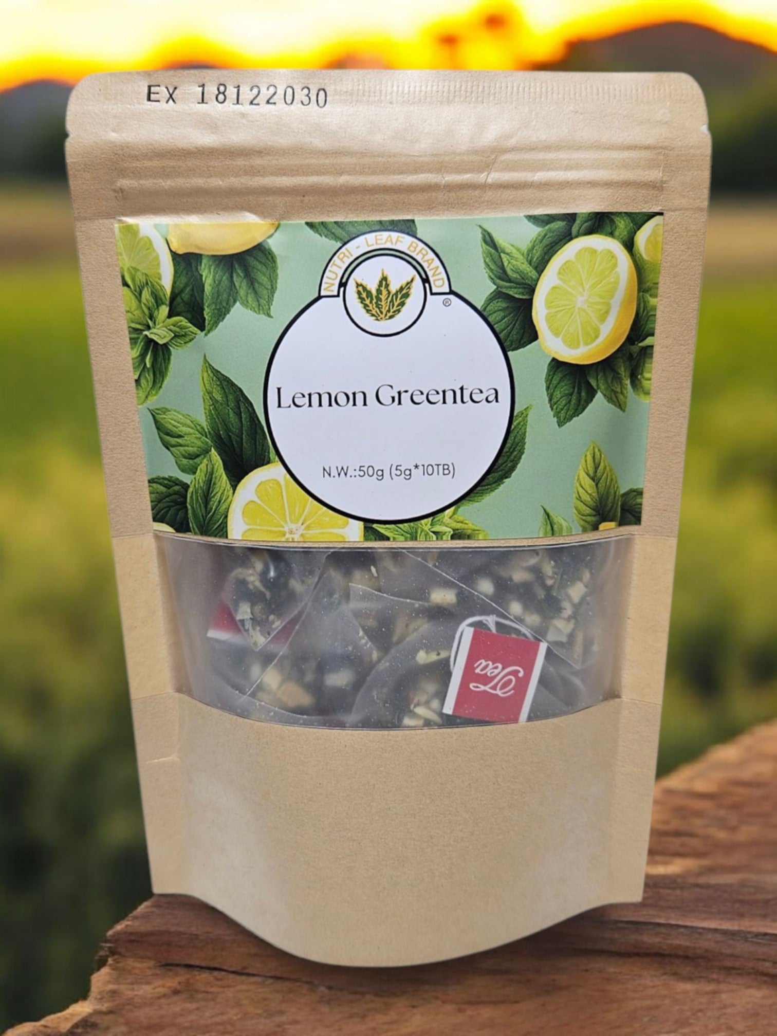 A standing pouch of Nutri-Leaf Brand Lemon Green Tea with a clear window showing tea leaves inside. The packaging is predominantly green with images of lemons and text detailing the product name and additional information.