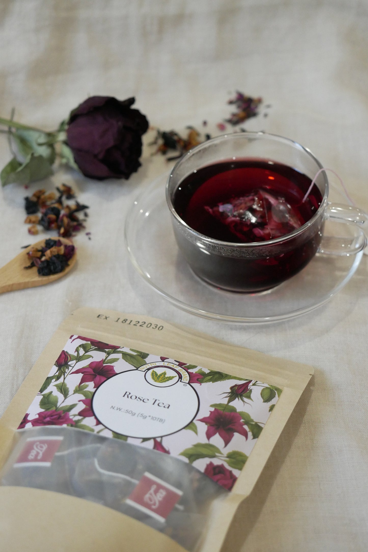 Tea bag with floral design next to a glass of red tea on a textured surface.